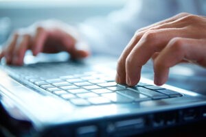 Close-up image of a person’s hands typing on a laptop keyboard