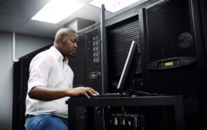 IT engineer working on a laptop in a server room to diagnose and prevent system downtime